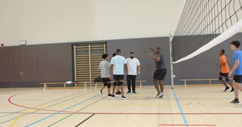 Diverse male volleyball team practicing indoors with coach guiding block and teamwork