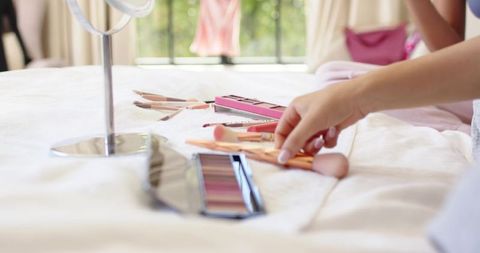 African american woman reaching for makeup brush on sunlit bed during morning routine