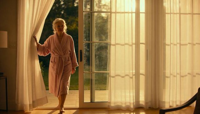 Senior woman stepping through sliding door in pink bathrobe, peaceful morning light