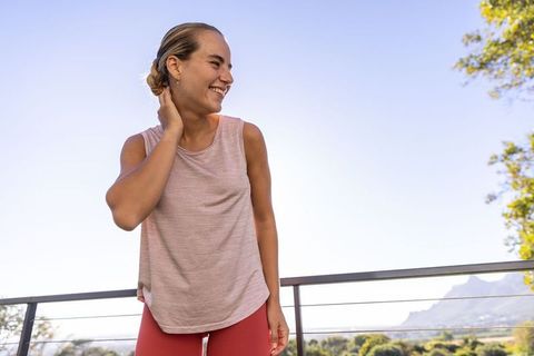 Smiling woman standing on balcony touching neck wearing red leggings and hoop earrings