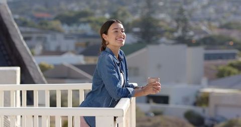 Woman Relaxing on Balcony with Scenic View Holding Coffee