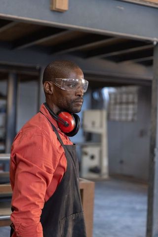 Senior african american technician wearing safety goggles and ear protection inspecting machinery
