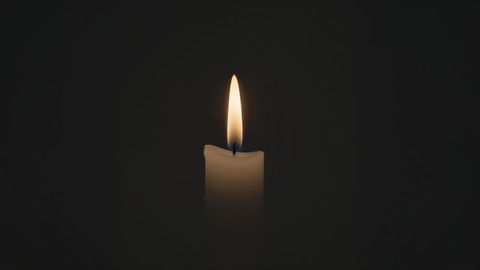 Glowing candle flame against black background for contemplative ambience and condolences