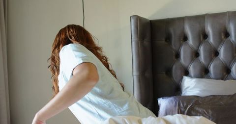 Redhead woman leaning on bed turning left wearing light short-sleeve tee in daylight