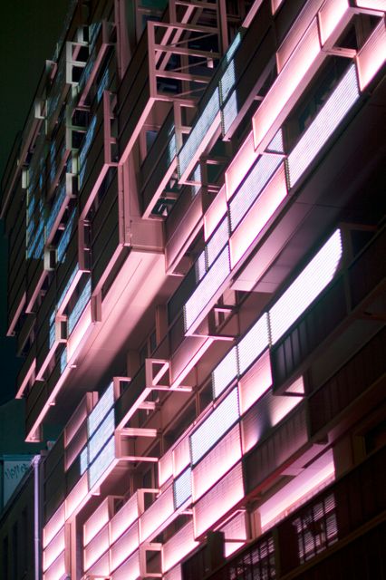 Modern building facade illuminated with vibrant neon lights during nighttime. The contemporary architectural design features a series of geometric patterns and bright neon lighting, highlighting the urban landscape. Perfect for showcasing cutting-edge architectural projects, city life, and night photography themes. Ideal for use in magazines, urban development presentations, or architectural design inspiration.
