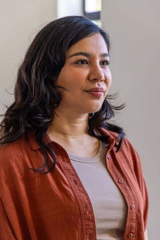 Thoughtful woman in rust shirt looking sideways in soft-lit minimalist interior portrait