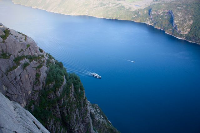 Aerial shot capturing boats cruising tranquil blue waters in a fjord surrounded by rocky cliffs. Ideal for travel advertisements, outdoor adventure promotions, and nature conservation campaigns.