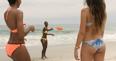 this scene captures a diverse group of women in vibrant bikinis playing frisbee on a sandy beach. the backdrop of the ocean adds to the summery and carefree atmosphere, making it perfect for promoting brands related to travel, beachwear, fitness, or lifestyle. ideal for marketing materials aiming to emphasize fun, diversity, and active lifestyle in summertime settings.