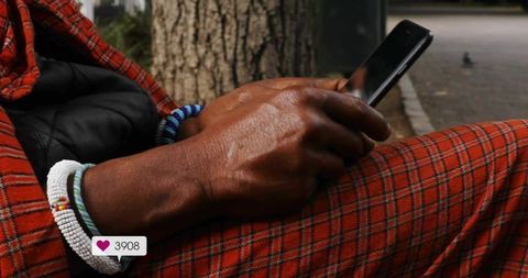 Man scrolling smartphone wearing red plaid pants and beaded bracelets on park bench