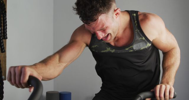 Man working out intensively on exercise bike, showcasing determination and physical effort. Useful for fitness promotions, gym advertisements, motivational content, and blog posts about physical training and perseverance.