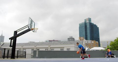 Rooftop basketball player dribbling toward hoop with cloudy city skyline and urban court