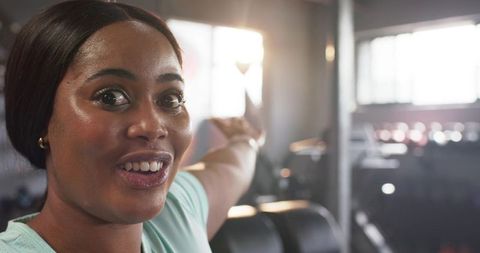 Energetic african american woman pointing to gym equipment, sunlit workout motivation