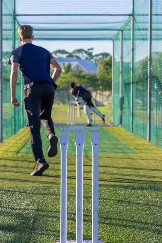 Cricket net practice with bowler running and batter striking ball behind white stumps outdoors