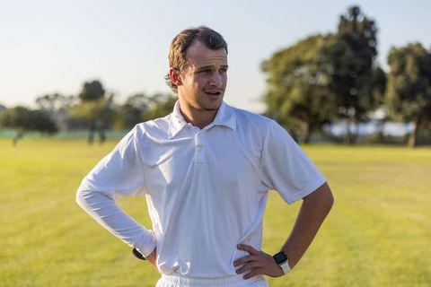 Cricket player standing hands on hips wearing white kit and smartwatch at golden hour