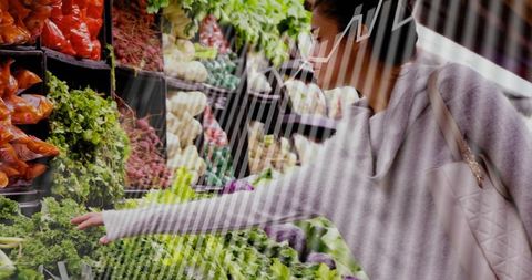 Masked woman selecting fresh leafy greens in supermarket while carrying quilted shoulder tote