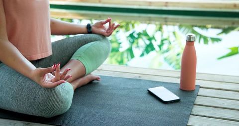 Woman Meditating Outdoors by Water with Smartphone and Water Bottle
