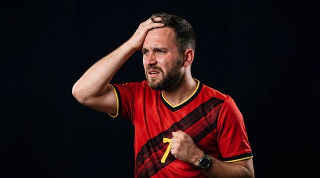 Frustrated soccer fan holding head and clenching fist while wearing red number 7 jersey