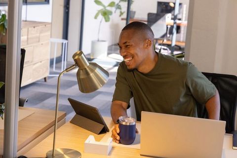 African american professional laughing at modern coworking desk with laptop and tablet