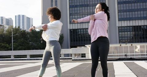 Two women stretching on urban rooftop plaza warming up for outdoor fitness workout