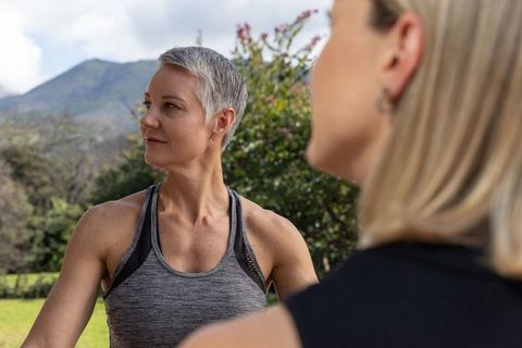 Mature woman exercising outdoors with friend on grassy lawn near mountain ridge