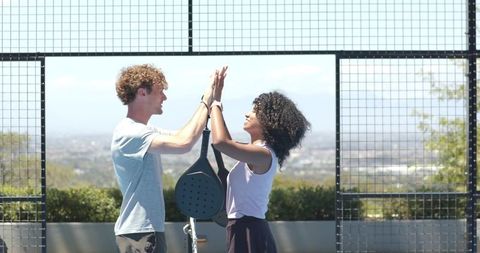 Rooftop padel partners high-fiving after match with urban skyline background