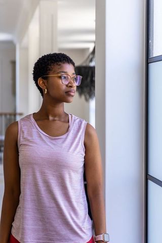 Contemplative african woman gazing by frosted glass in modern minimal corridor with glasses