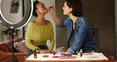Makeup artist applying lip color on model during home beauty session with ring light