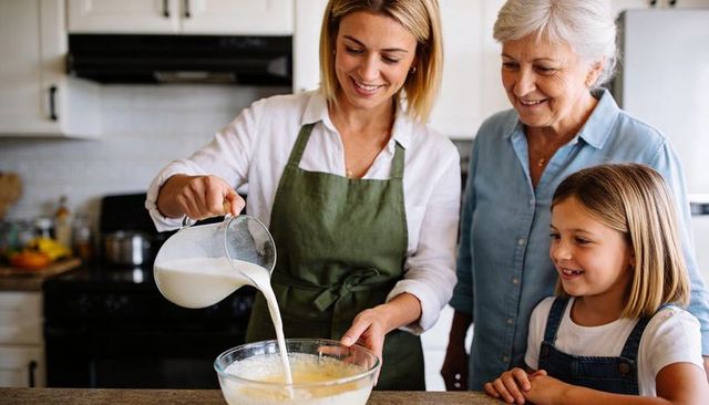 Family baking together pouring milk into batter with grandmother and child smiling
