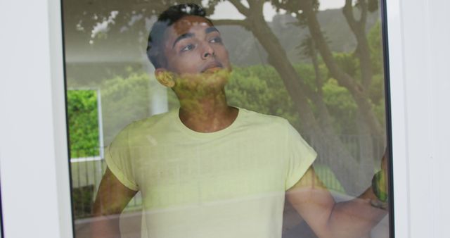 Portrait of biracial man standing and looking out of window. staying at home in isolation during quarantine lockdown.