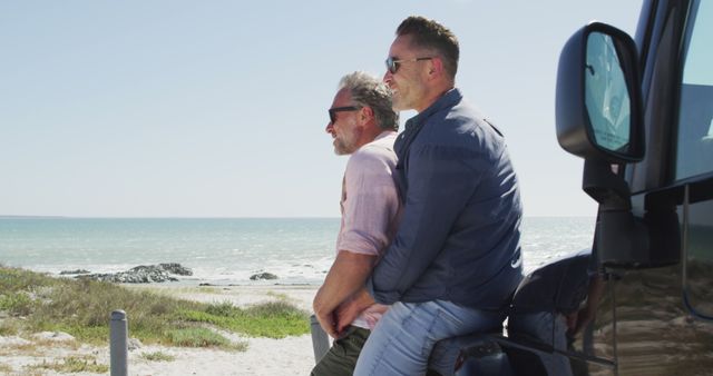 Couple embracing while enjoying a scenic view of the beach and ocean on a sunny day. Both wearing sunglasses and casual clothing, leaning against a vehicle. Ideal for themes related to vacations, relaxation, love, tranquility, beach outings, and outdoor leisure activities.