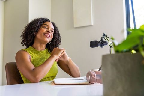 African american woman recording podcast in bright home studio with microphone notebook