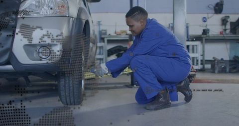 Crouching mechanic tightening SUV wheel with breaker bar in workshop blue coveralls