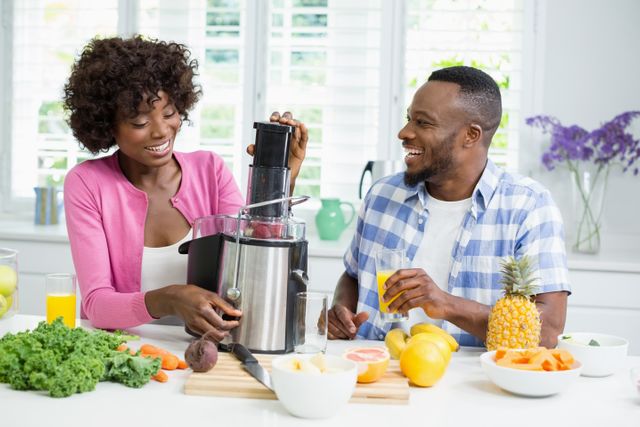 Couple enjoying time together while preparing a healthy smoothie in a bright, modern kitchen. Ideal for use in articles or advertisements related to healthy living, nutrition, family activities, and home appliances. Perfect for promoting kitchen gadgets, juicers, and healthy lifestyle choices.