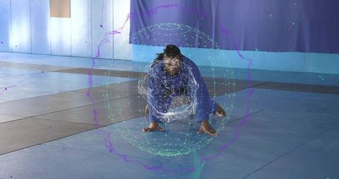 Martial artist crouching with holographic training sphere wearing blue gi on gym mat