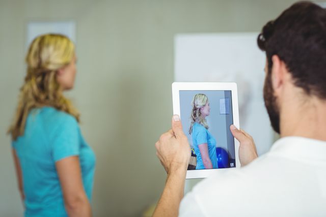 Physiotherapist using a digital tablet to take a photograph of a patient in a clinical setting. Useful for illustrating modern medical practices, healthcare technology, patient treatment, and professional medical environments.