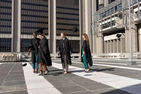 Female graduates celebrating on urban rooftop tossing mortarboards and holding diplomas