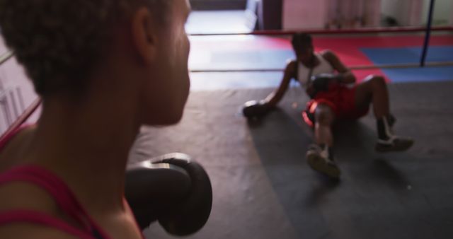 Boxers inside a gym training ring during a workout session. One boxer is resting in the foreground while another is seen lying on the ground. Ideal for illustrating fitness training, athletic determination, sports competition, and teamwork. Useful for blogs, fitness articles, sports training guides, and motivational content.