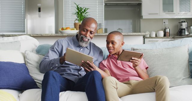Image of happy african american father and son using tablets together. Family, spending quality time together at home.