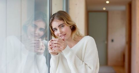 Woman enjoying cozy moment with ceramic mug by window