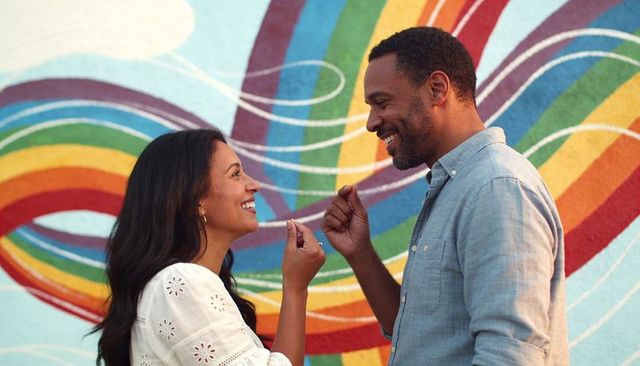 Playful couple sharing intimate moment in front of vibrant rainbow mural, urban street art backdrop