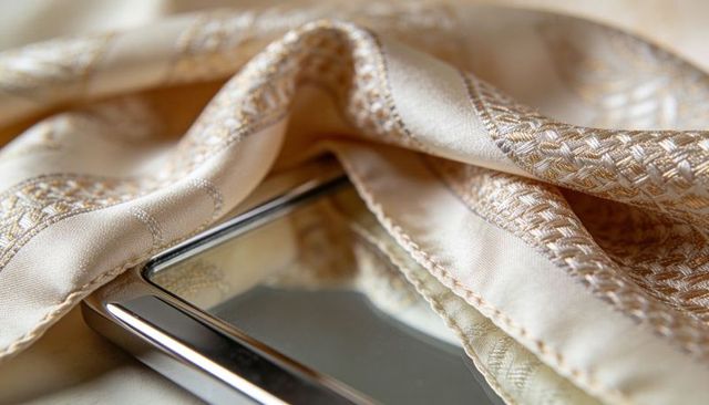Rectangular handheld mirror resting among cream-gold embroidered satin reflecting detail