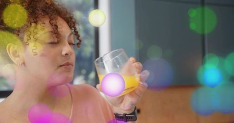 Curly-haired woman smelling glass of orange juice, enjoying calm mindful morning routine