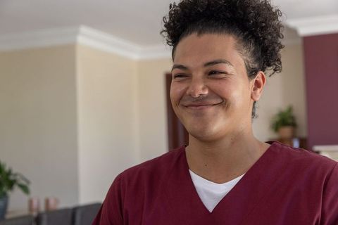Smiling male caregiver wearing maroon scrubs in cozy home living room