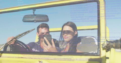 Young couple taking selfie in yellow convertible with code overlay, digital nomad road trip