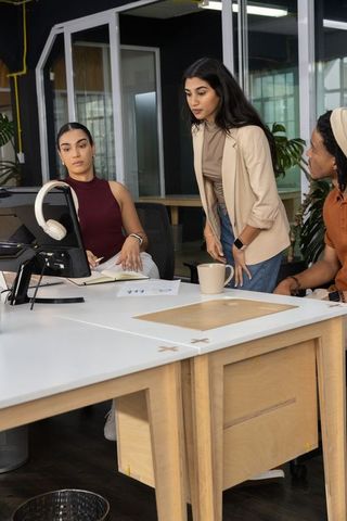 Multicultural team collaborating at shared desk using monitor and headphones in modern coworking spa