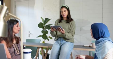 Diverse women brainstorming and presenting ideas using tablet in modern coworking office
