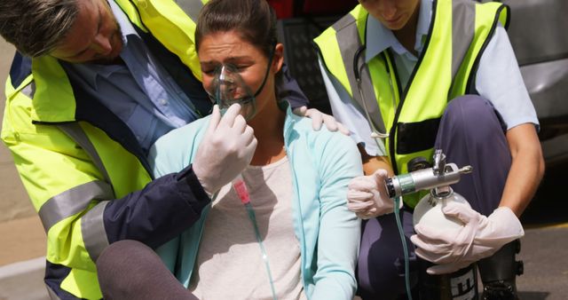 Two emergency responders assist a young woman by administering oxygen. The patient appears distressed, and the scene takes place outdoors. Useful for illustrating medical emergencies, first aid training, paramedic services, healthcare support, and crisis response visuals.