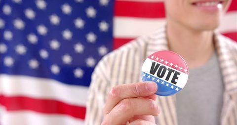 Person holding vote badge with american flag backdrop