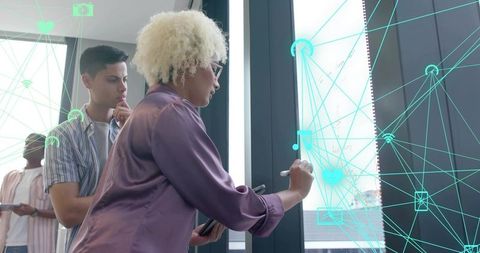 Woman annotating glass wall using stylus and tablet with ar network overlay