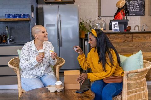 Diverse women sharing coffee and cupcakes in cozy cafe, laughing and enjoying casual chat